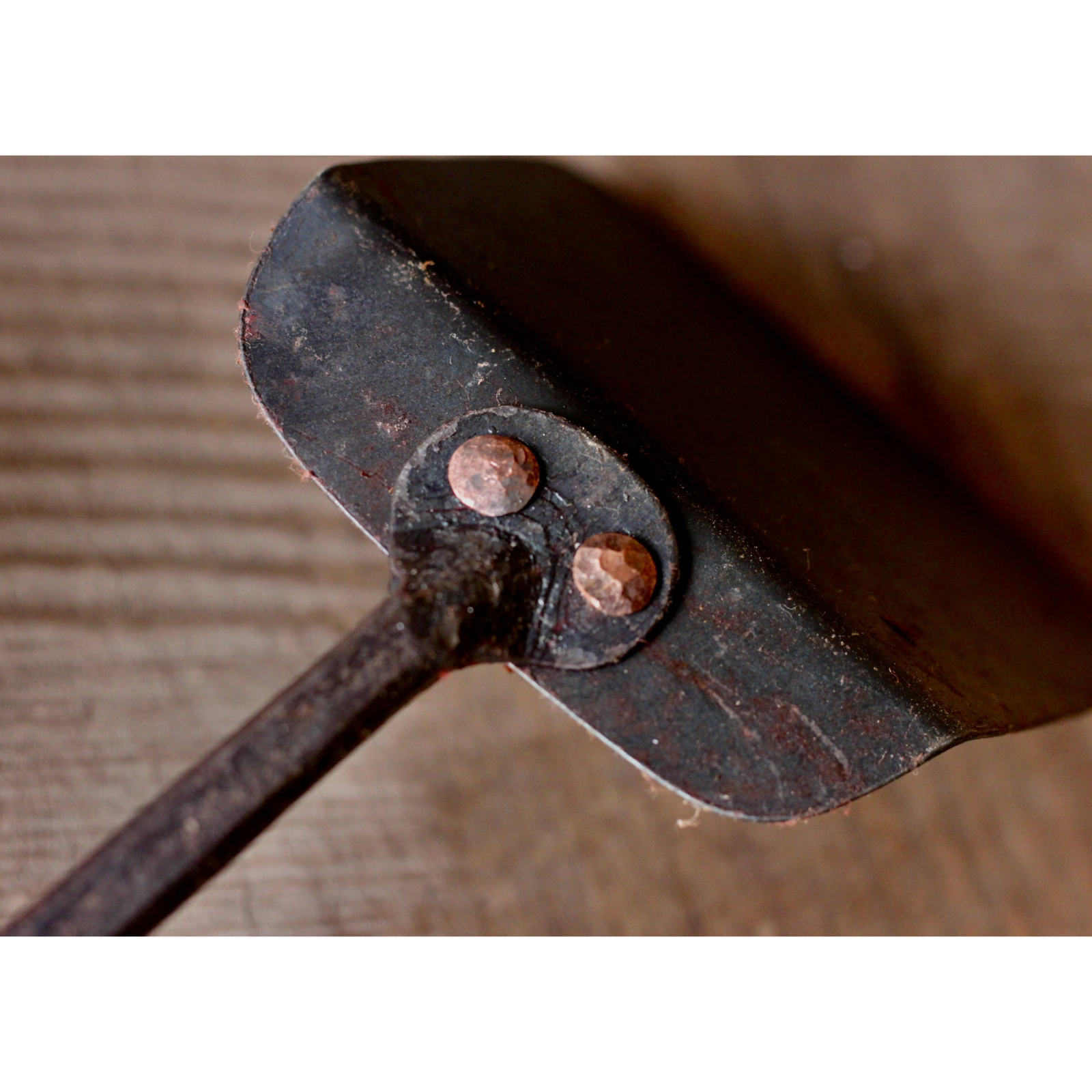 Close-up of a metal object with two rivets on a wooden surface