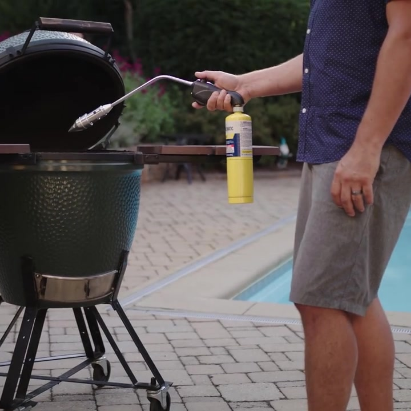 Man in polka dot shirt and shorts lighting big green egg with rocketfire torch
