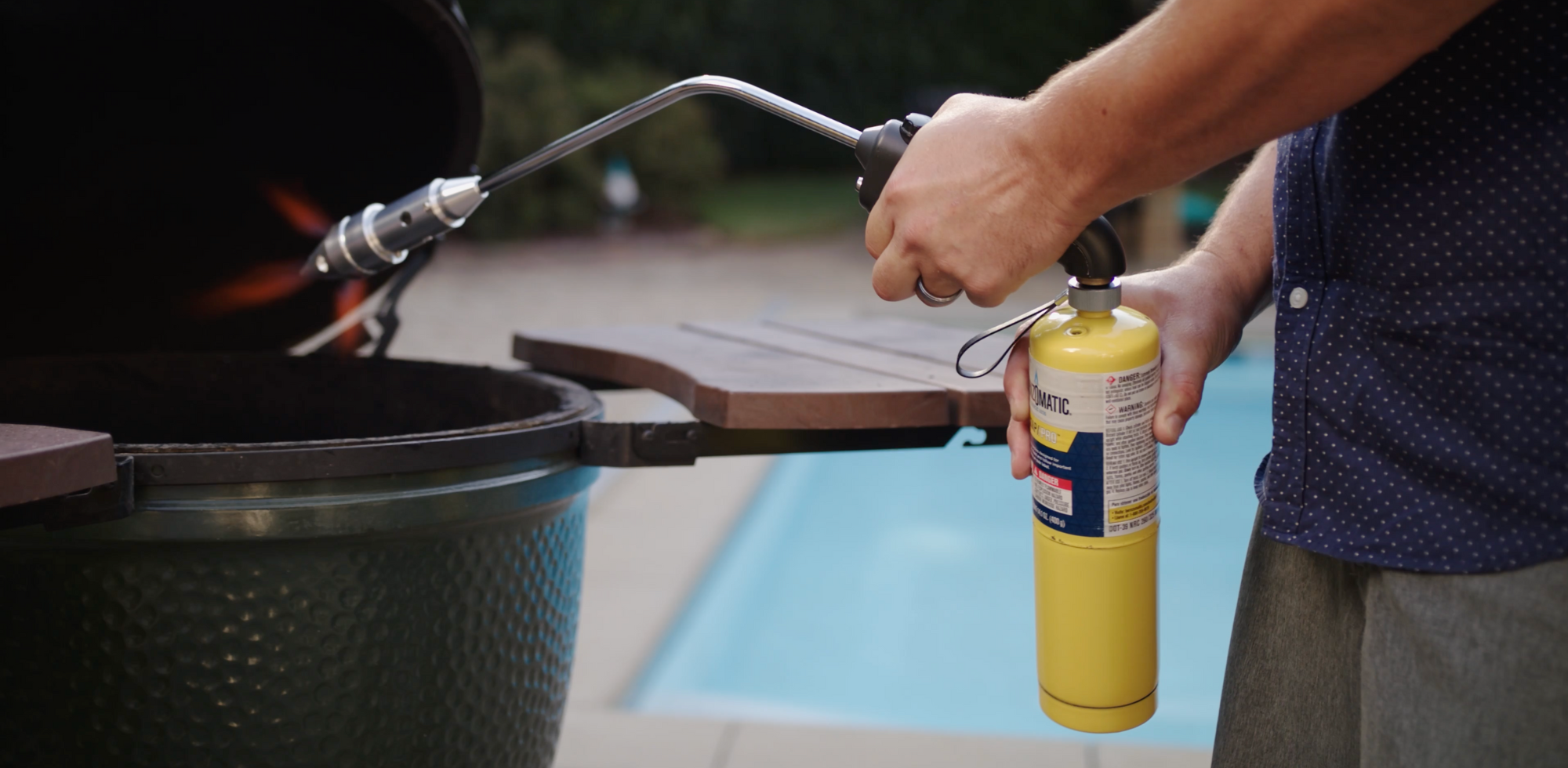 Man in polka dot button down lighting big green egg with rocketfire torch