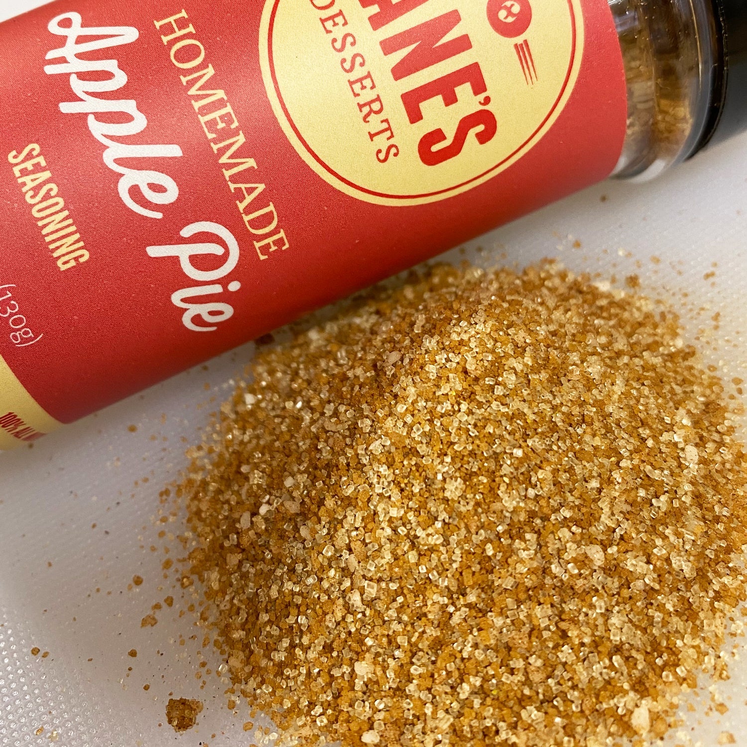 Bottle of 'Hane's Homemade Desserts Apple Pie Seasoning' with spilled seasoning on a white surface