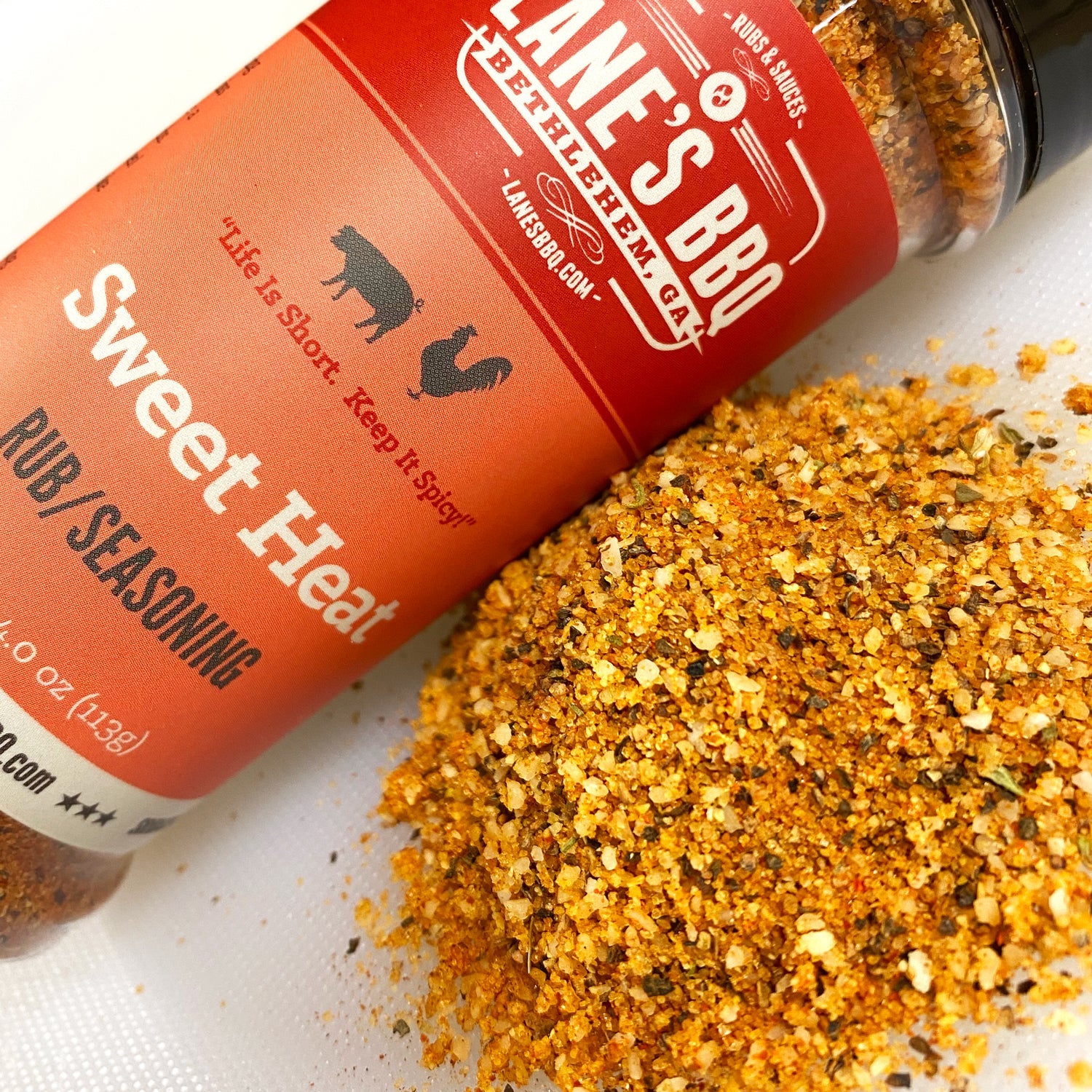 Jane's BBQ Sweet Heat seasoning bottle with spilled seasoning on a white surface