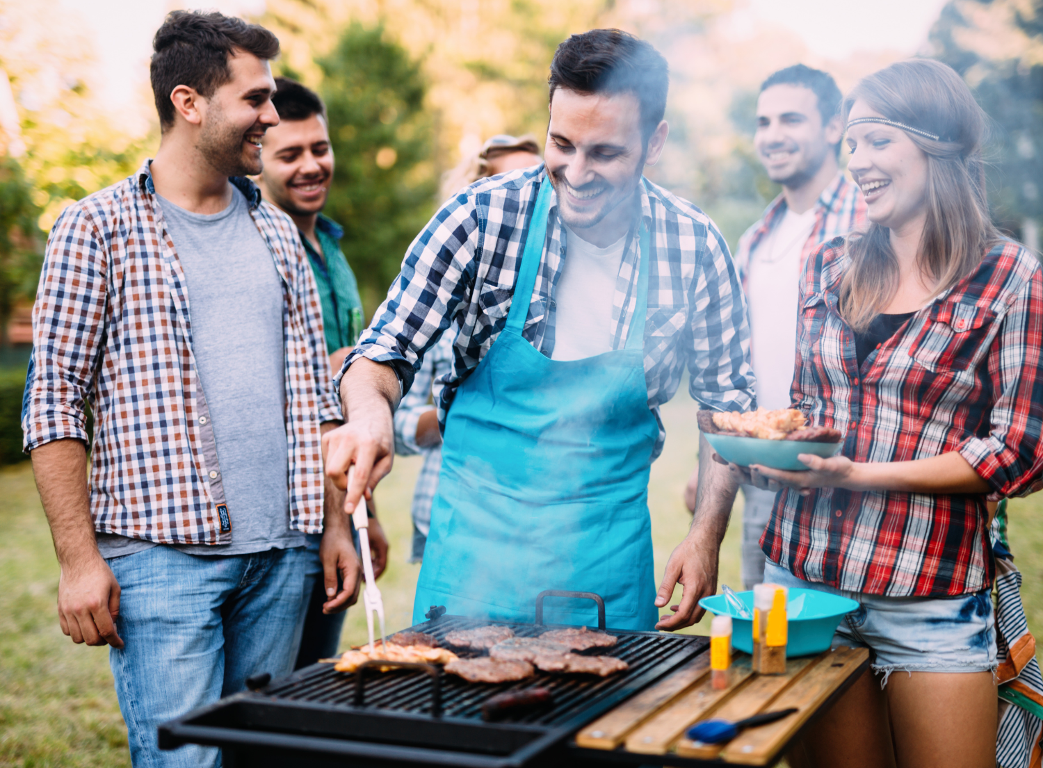 a group of friends standing in front of a grill cooking hamburgers