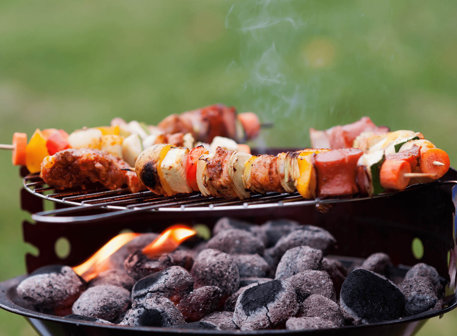 Meat and vegetable shish kebab grilling overtop a charcoal grill 