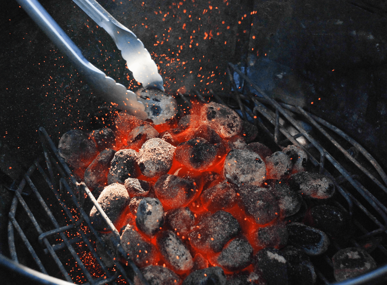 a mound of charcoal briquettes stacked in a grill lit with an orange flame