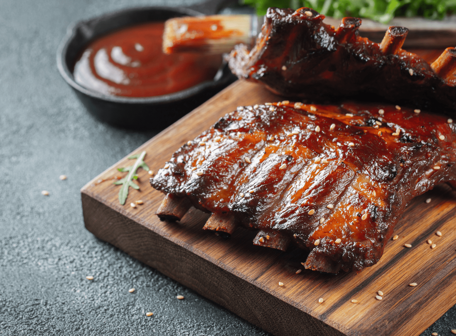 A rack of bbq ribs on a wooden cutting board with a small bowl of bbq sauce on the side