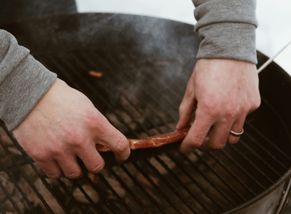 Man placing meat on lit charcoal grill