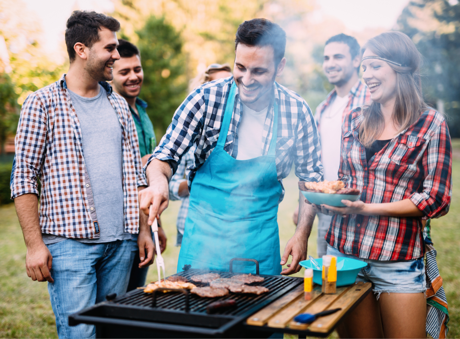 A group of friends cooking and laughing around a open grill