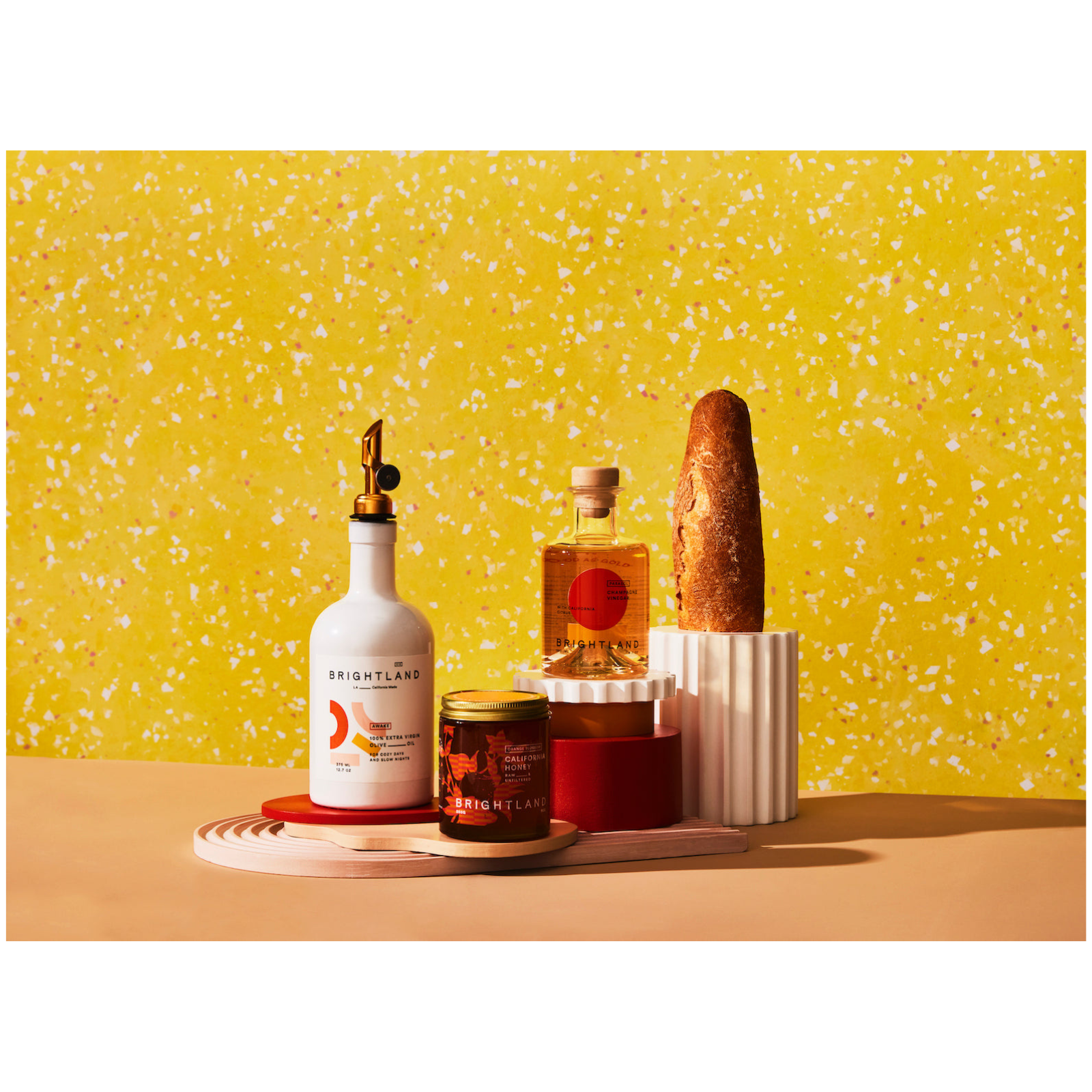 Assorted products including a bottle, jar, and loaf of bread on a yellow speckled background