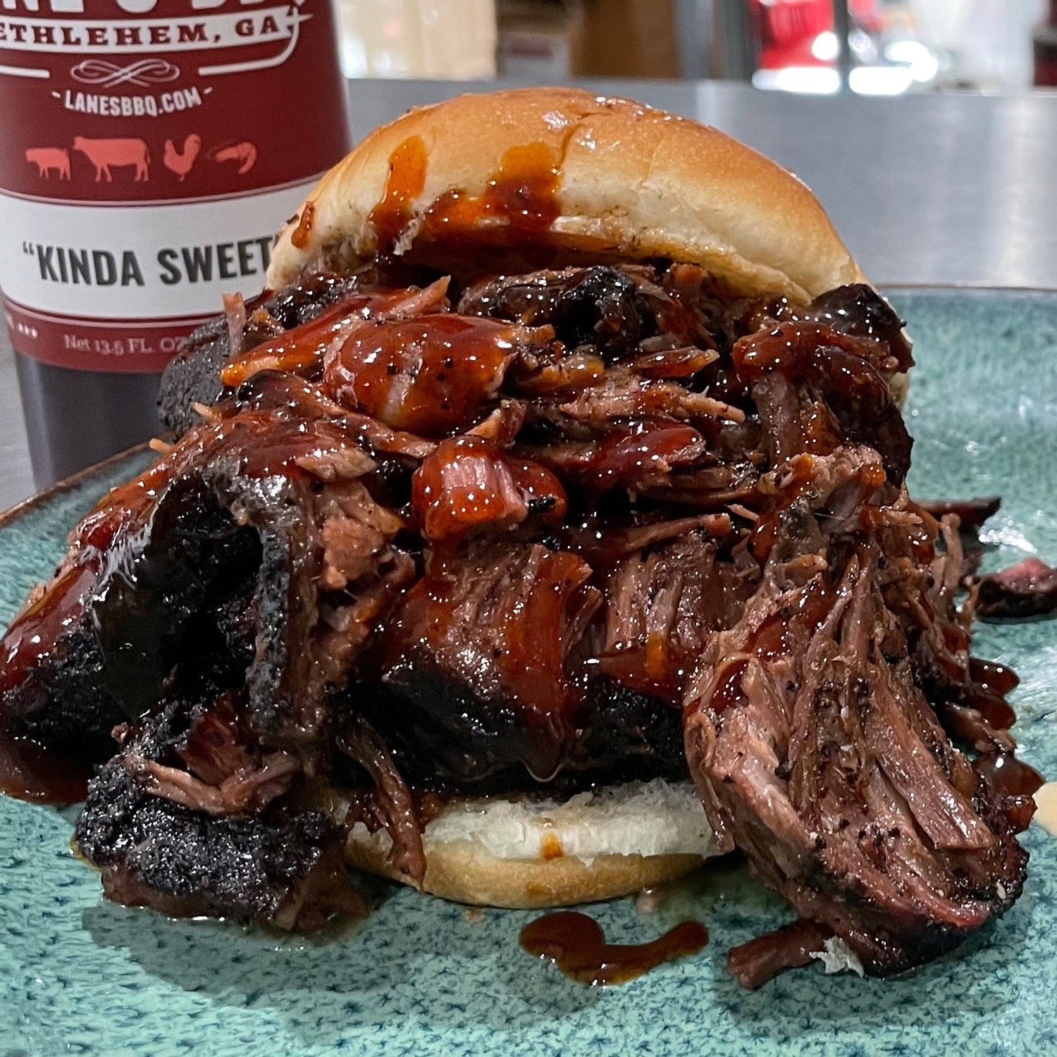 Barbecue sandwich with pulled meat on a bun, accompanied by a bottle of barbecue sauce in the background.
